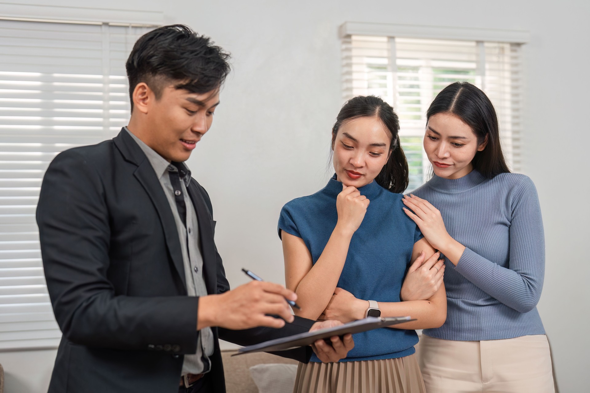 Real estate agent writing down information while two potential buyers look on in a modern setting.